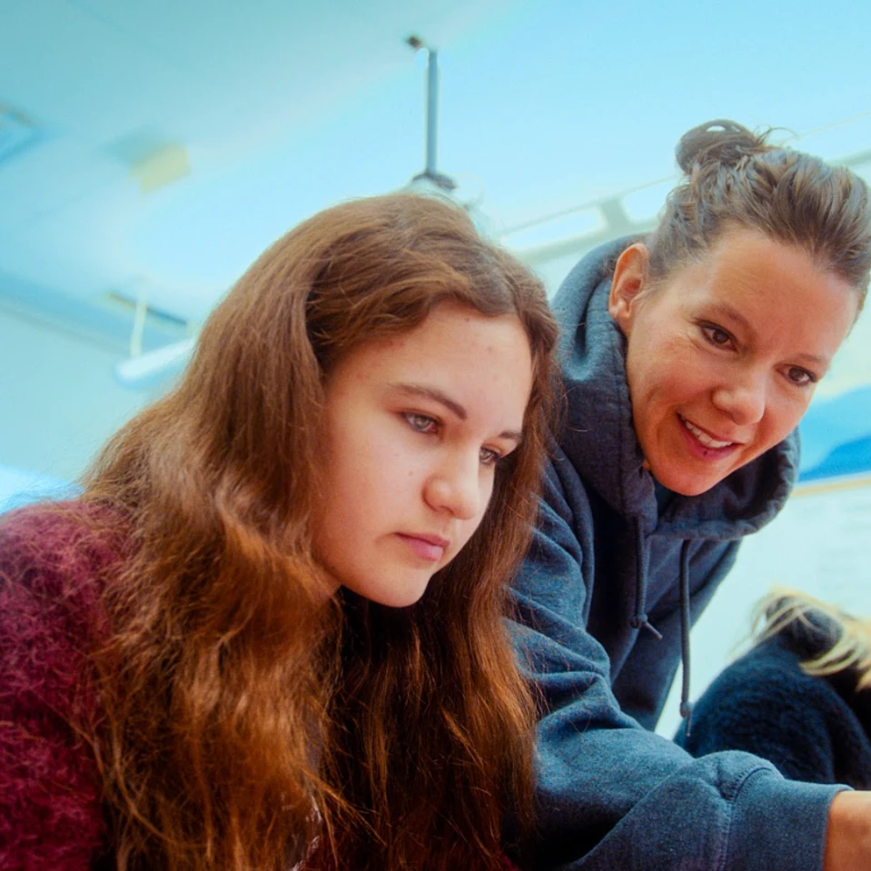 une enseignante pointe quelque chose à une élève assise à son bureau