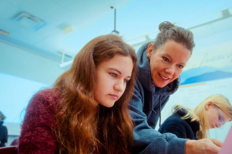 une enseignante pointe quelque chose à une élève assise à son bureau